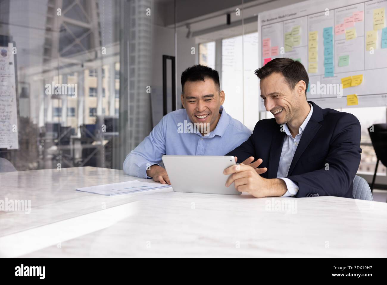 Friendly laughing two diverse businessmen discussing project insights using tablet Stock Photo