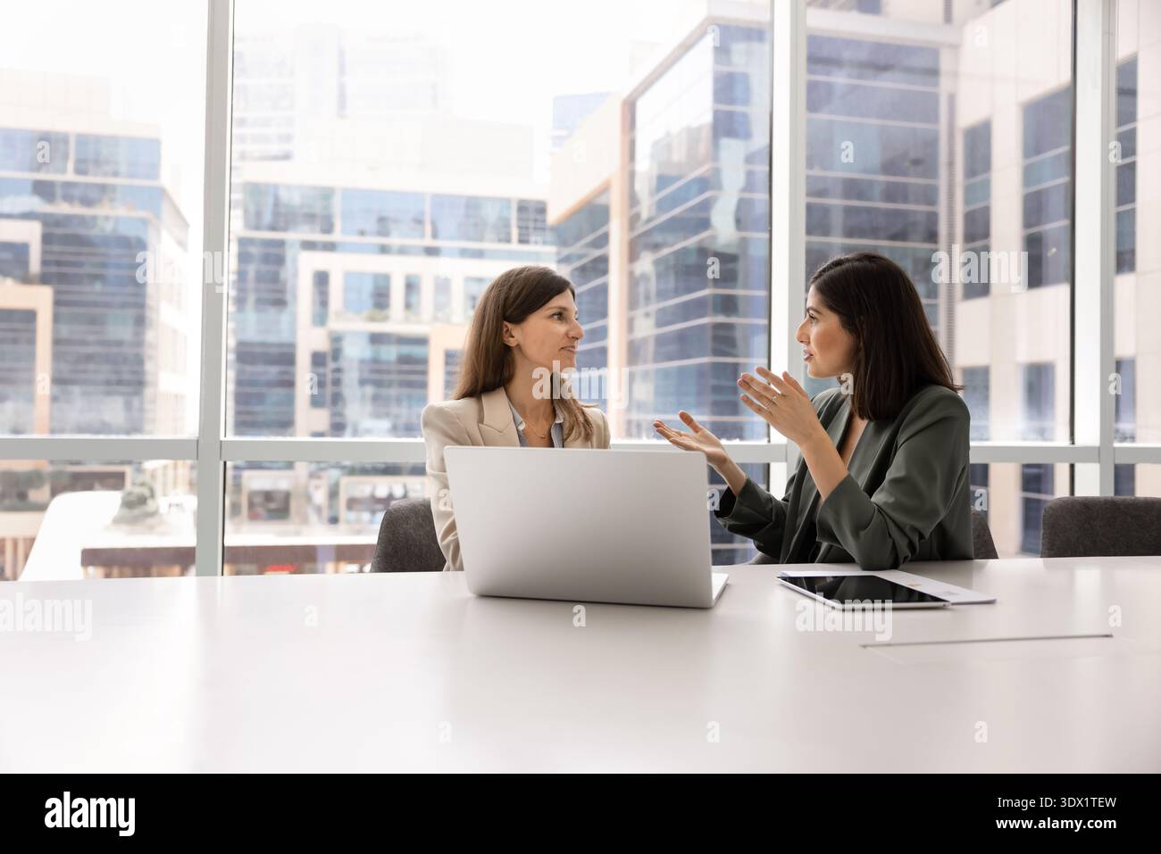 Two professional women having discussion in modern glass-walled boardroom Stock Photo