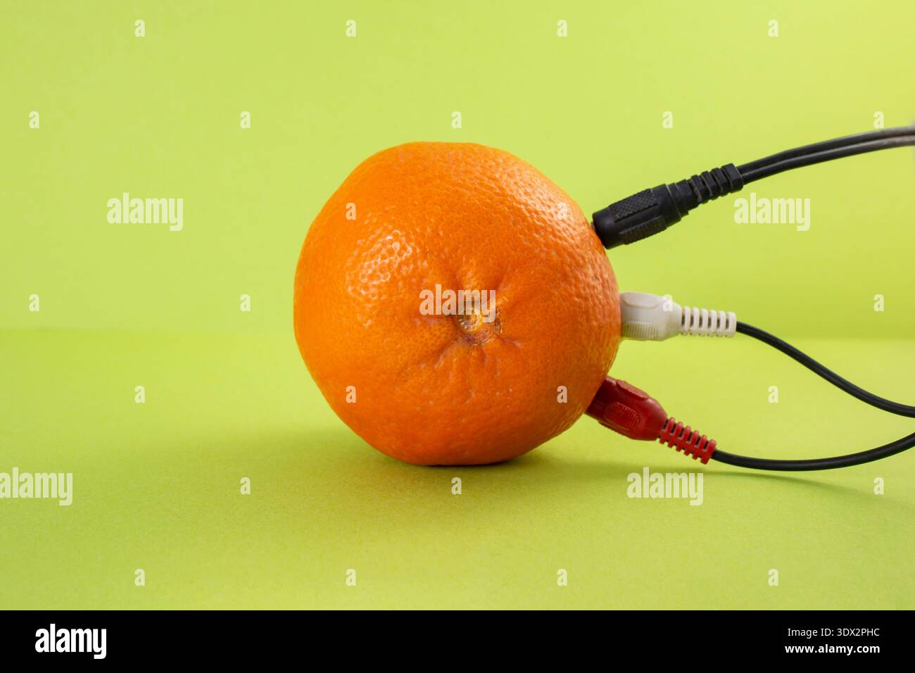Colorful cables plugged in a orange on bright green background, abstract energy concept Stock Photo