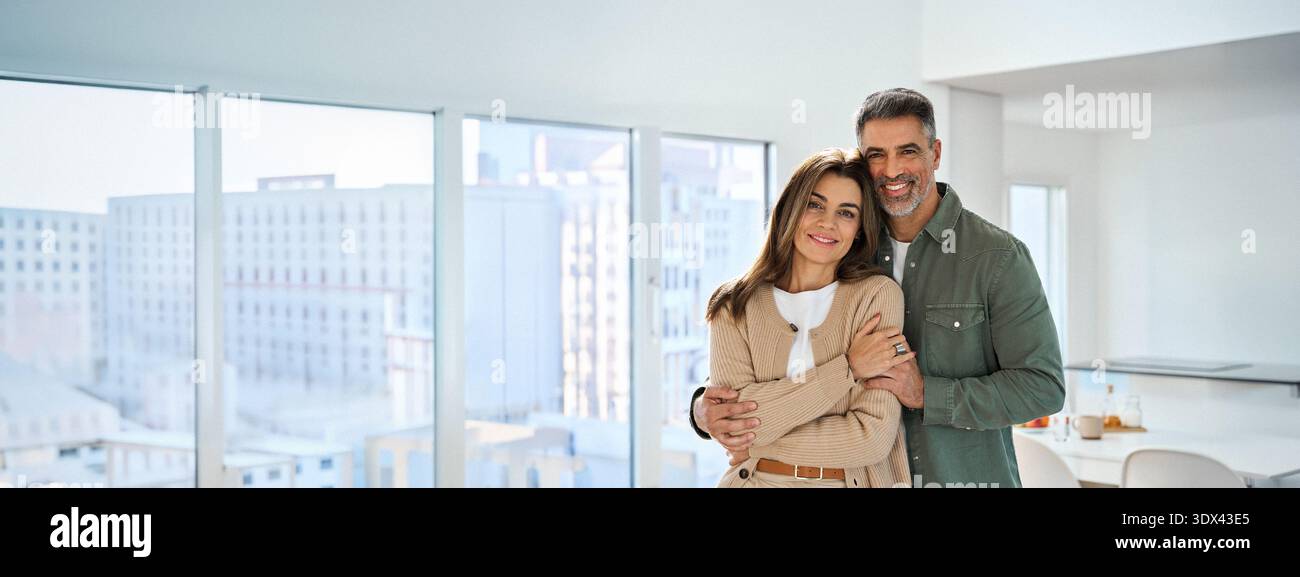 Happy mature couple hugging looking at camera standing in kitchen at home. Stock Photo