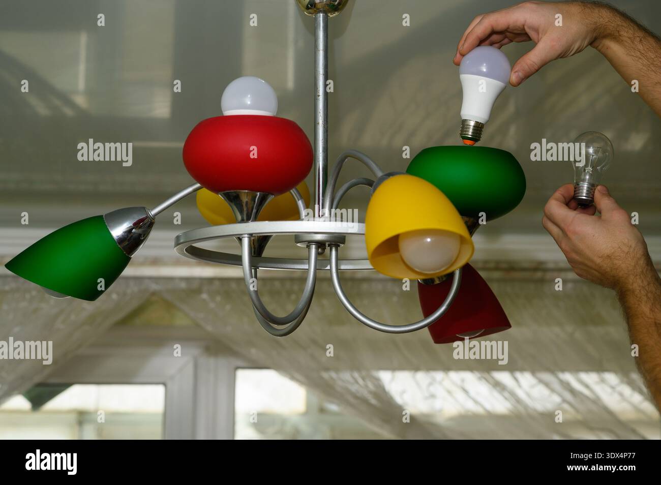 Man holding incandescent bulb and LED bulb before changing lamp.Lamp symbolizes energy transition,representing choice between old technology, modern s Stock Photo