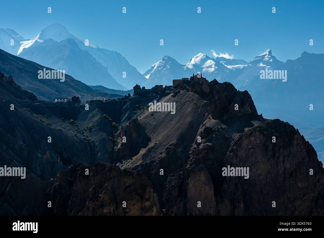 Dhankar Gompa on a ridge with the snow-capped Manirang peak and the Himalayan mountain range in the distance under a clear blue sky. Stock Photo