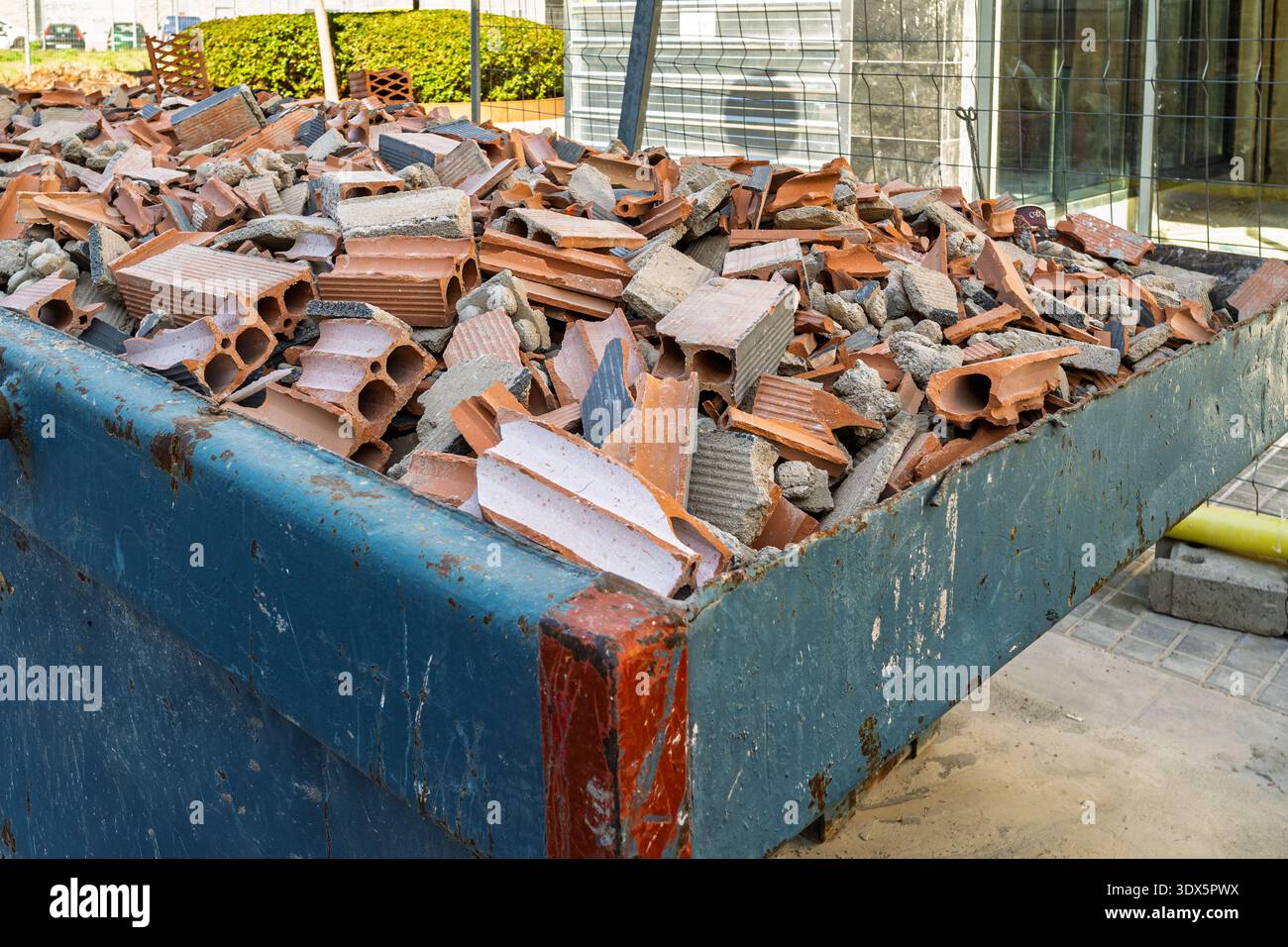 Close-up view of a metal skip container loaded with broken red hollow ...