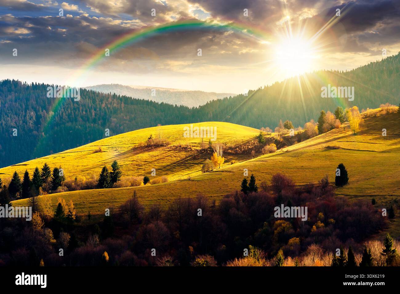 autumn landscape of rural region in mountains at sunset. rolling hills with green alps in dappled evening light. serene countryside under cloudy sky. Stock Photo