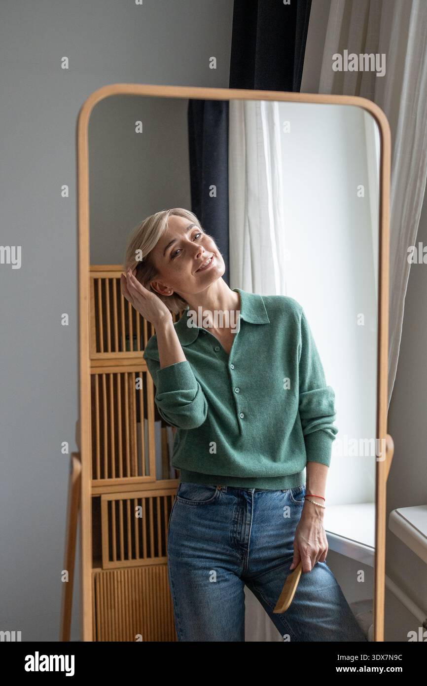 Cheerful smiling woman looking in mirror with positive expression, enjoying appearance in reflection Stock Photo