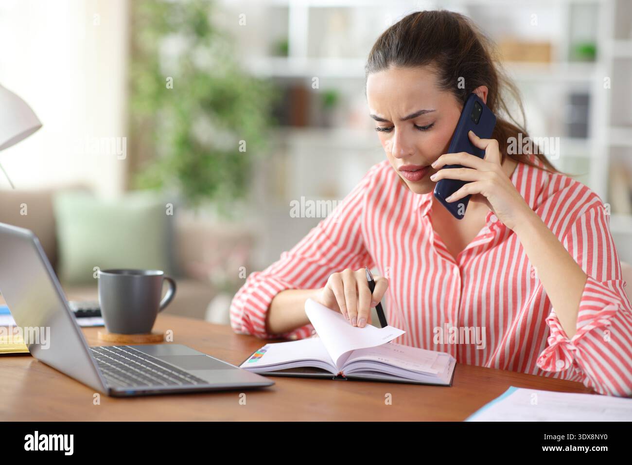 Stressed self employed checking agenda talking on phone working at home Stock Photo