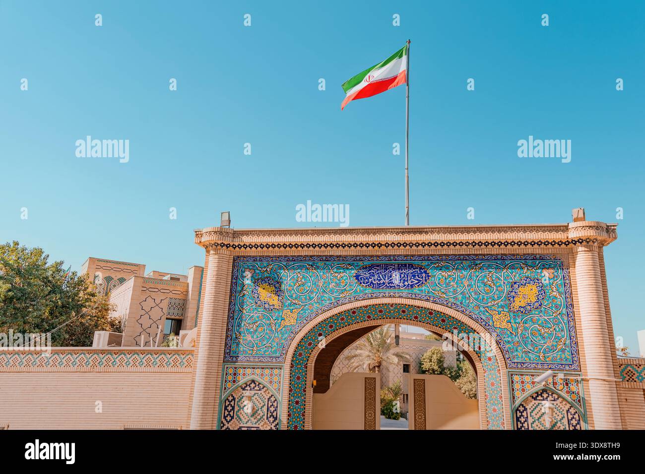 30 November 2025, Doha, Qatar: Iran flag waving on a pole above an architectural facade featuring intricate geometric tile patterns Stock Photo