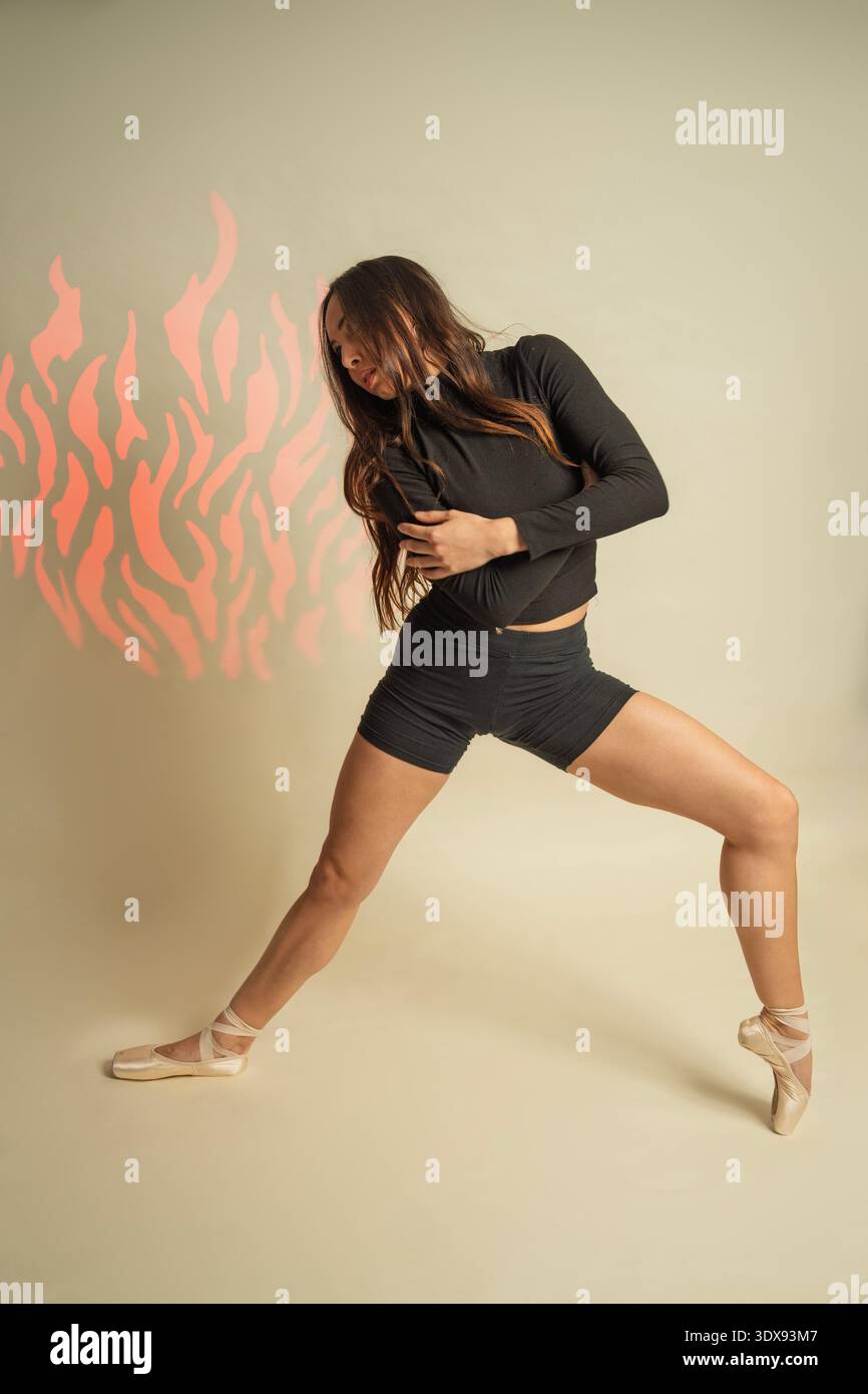 Female dancer performing a dynamic move, showing emotion and strength with projected flame pattern Stock Photo