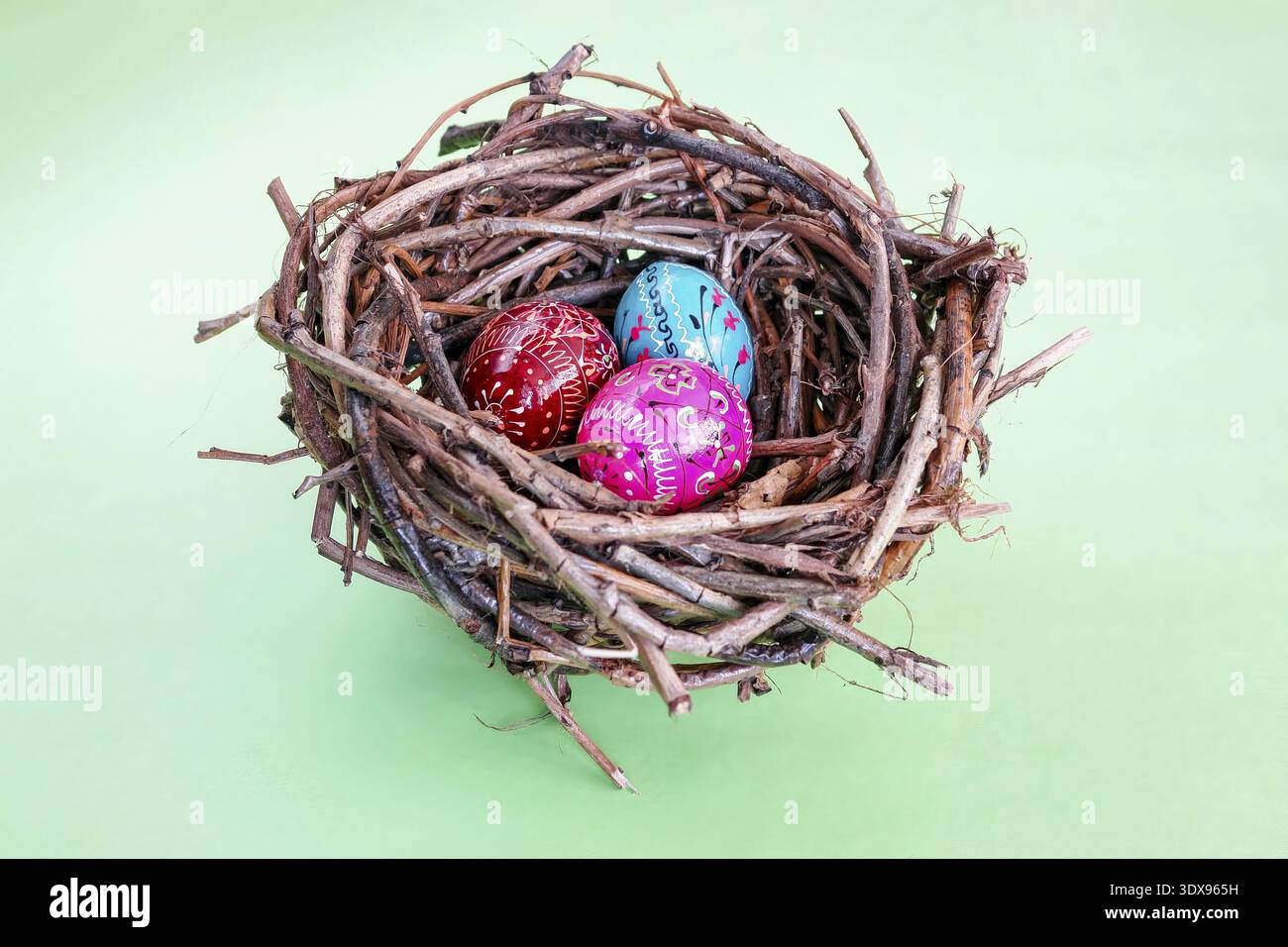 Three hand painted easter eggs in bird's nest over light green background Stock Photo