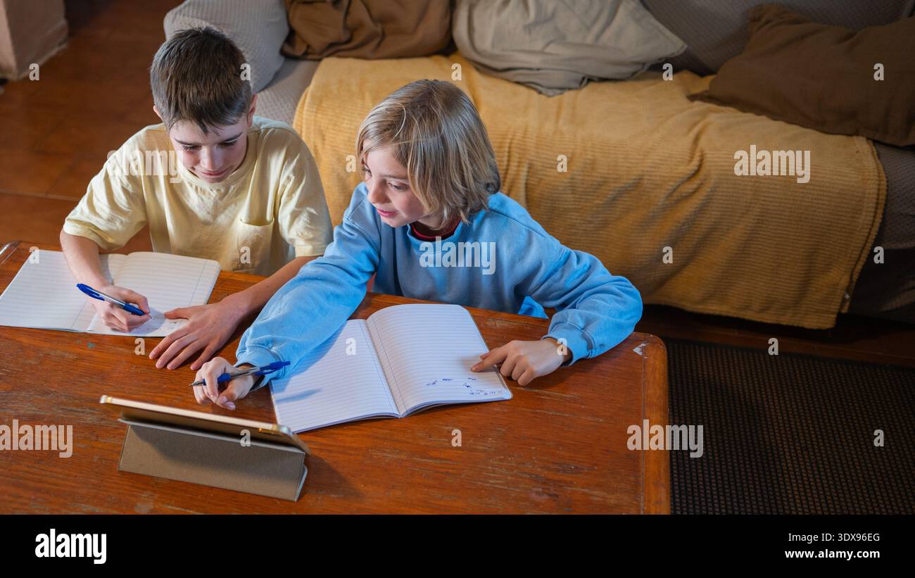 Two boys are studying and doing schoolwork at home, using a tablet and notebooks Stock Photo