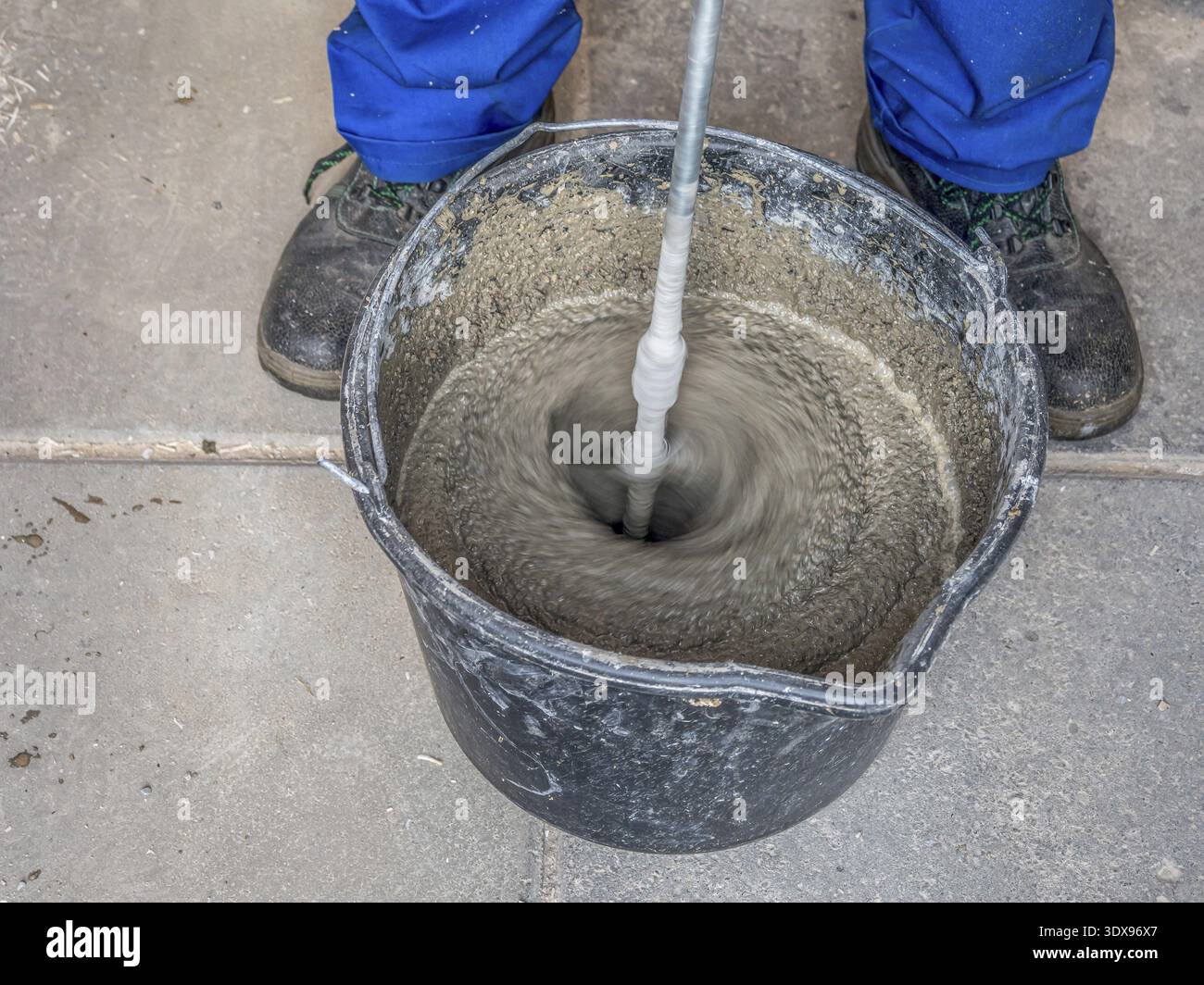Construction worker mixing mortar in a bucket using handheld concrete mixer Stock Photo