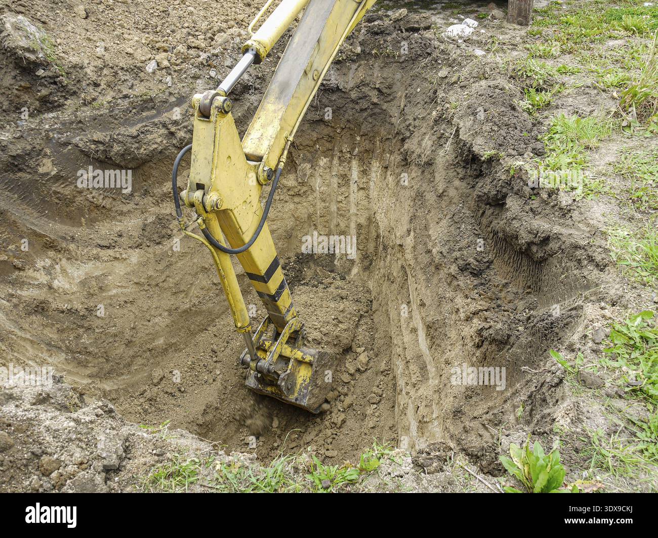 A yellow excavator digging a deep trench in the soil, showcasing heavy ...