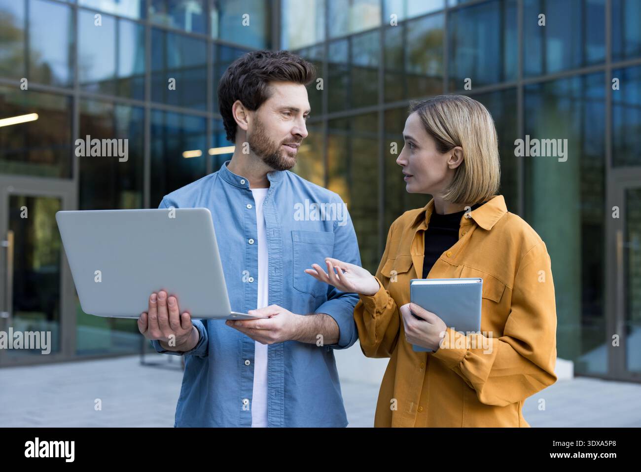 Startup team members having a productive business discussion and sharing ideas about a project while standing outside a modern office building, using a laptop and a tablet Stock Photo