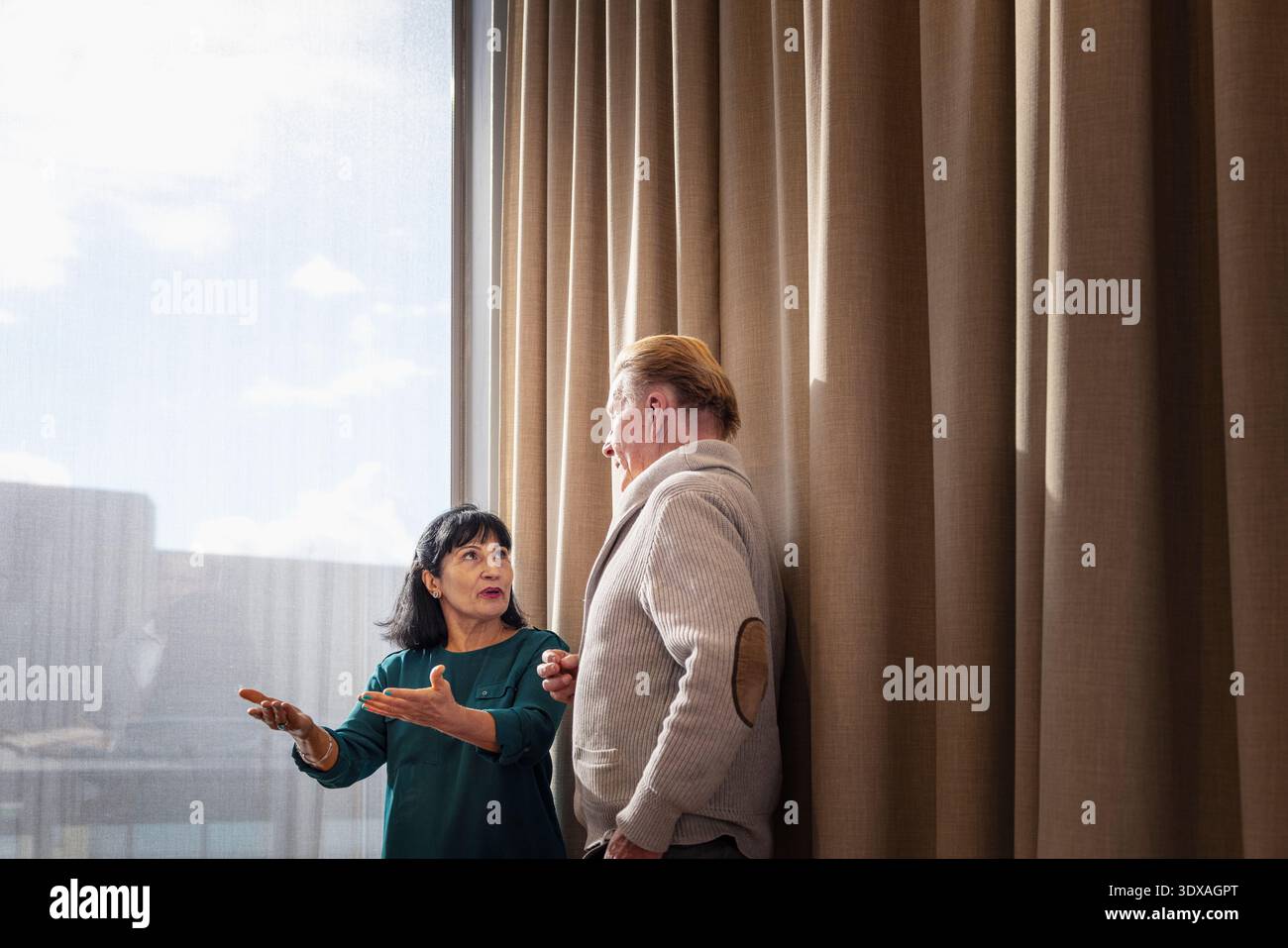 Senior businesswoman gesturing while explaining ideas to male coworker standing near window in office Stock Photo