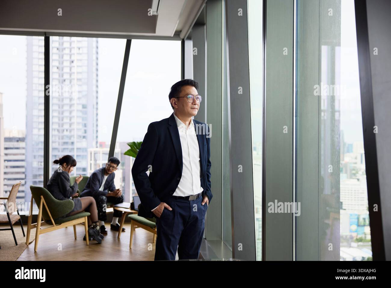 Confident businessman looking through window while standing with hands in pockets at office Stock Photo
