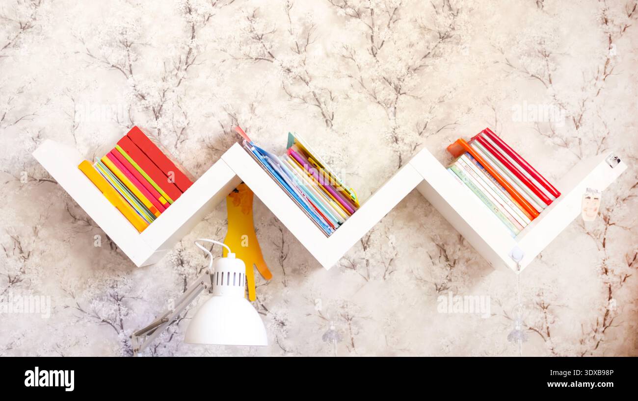 Zigzag bookshelf with books on a light wall Stock Photo