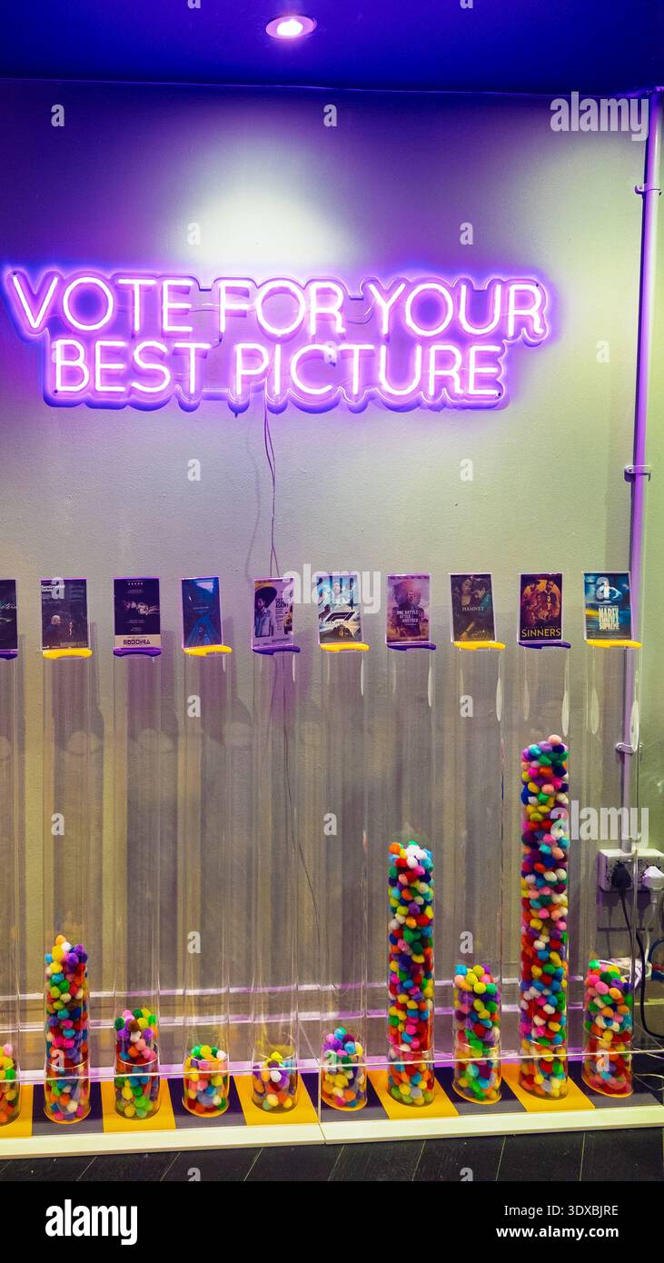 Vibrant Curzon Soho cinema interior with large pink neon “VOTE FOR YOUR BEST PICTURE” sign, colorful candy-filled acrylic columns, film posters and pu - Smartphone Captured Stock Image