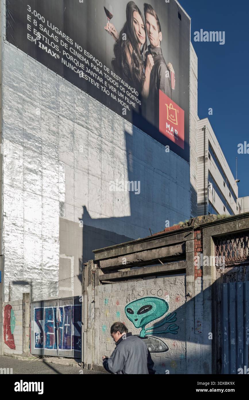 Large cinema advertisement on an urban building wall above a street with alien graffiti and a man walking by in Portugal. Stock Photo