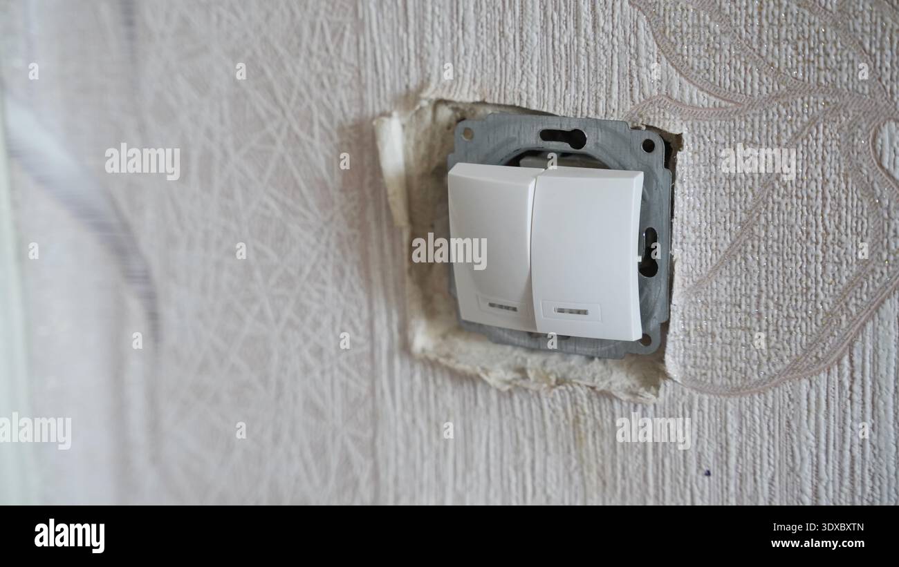 Double white wall light switch installed in textured wallpaper during interior renovation process. Stock Photo