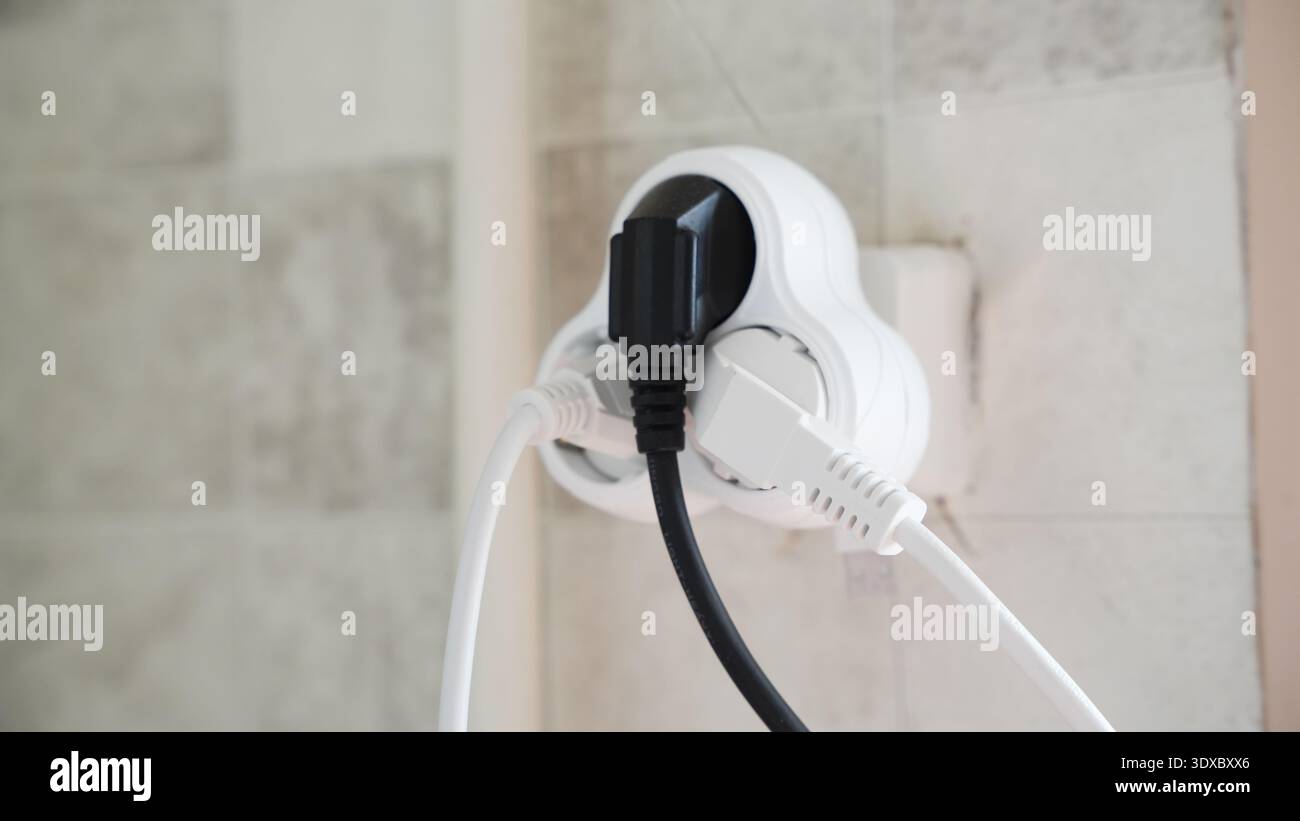 Multiple electrical plugs connected to a wall socket adapter in a tiled kitchen interior. Stock Photo