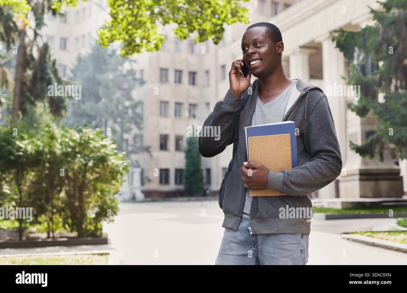 Student Talks on the Phone While Holding Notebooks in a University Courtyard During the Day Stock Photo