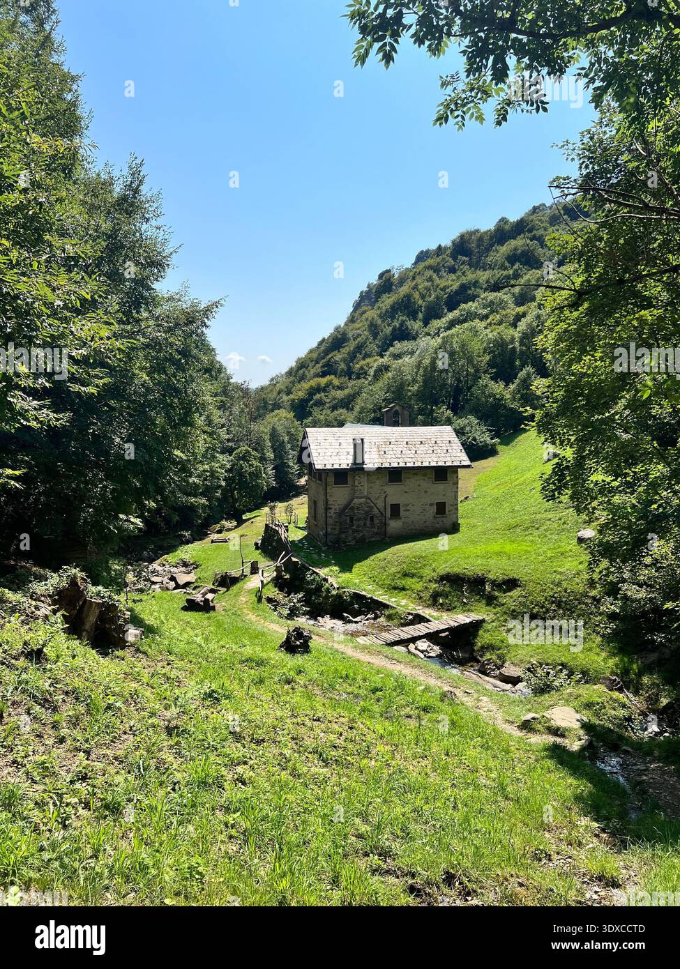 A traditional stone church and rustic building nestled in the lush green mountains of Mandello del Lario, overlooking Lake Lecca, Italy in summer. - Smartphone Captured Stock Image