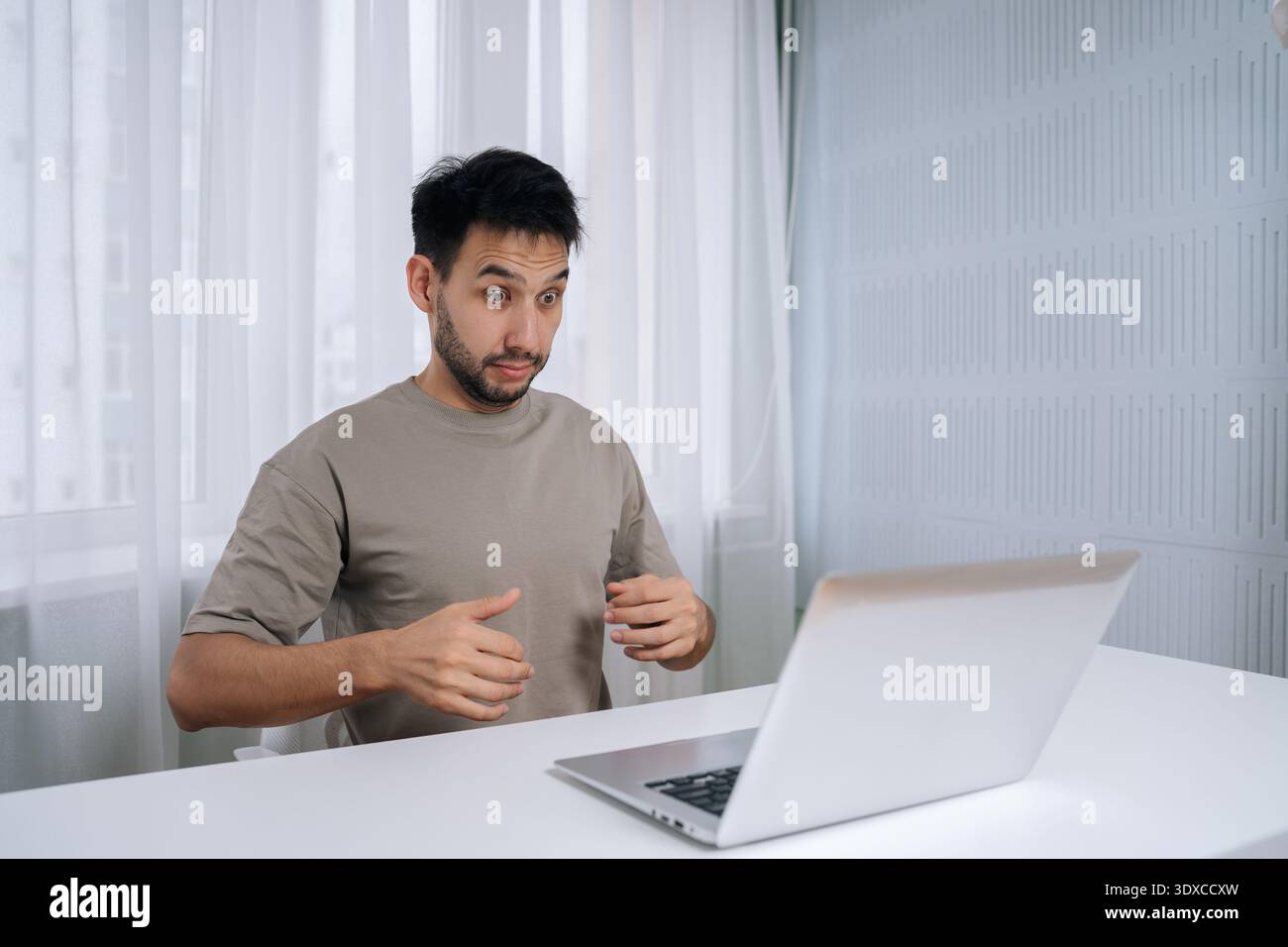 Shocker freelancer young man reacting with shock and confusion during remote work, experiencing technical problem or unexpected computer error while Stock Photo