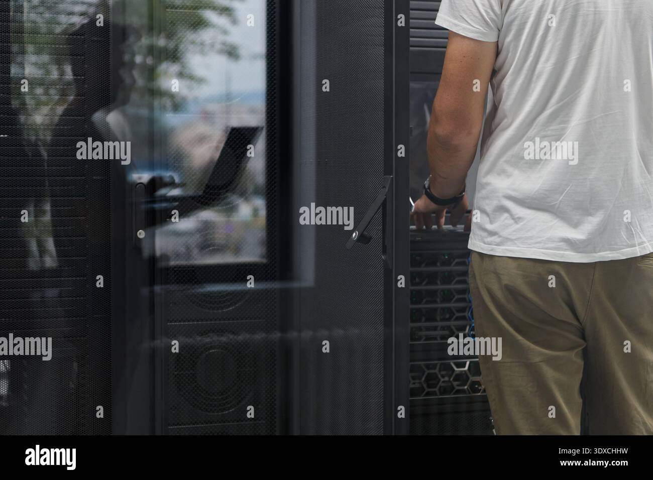 IT technician working on server rack in office data center with visible network equipment and reflection Stock Photo