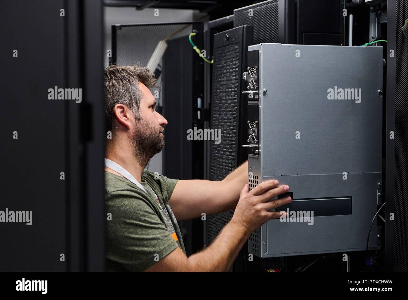 IT technician installing server hardware in a data center rack performing maintenance and network setup Stock Photo
