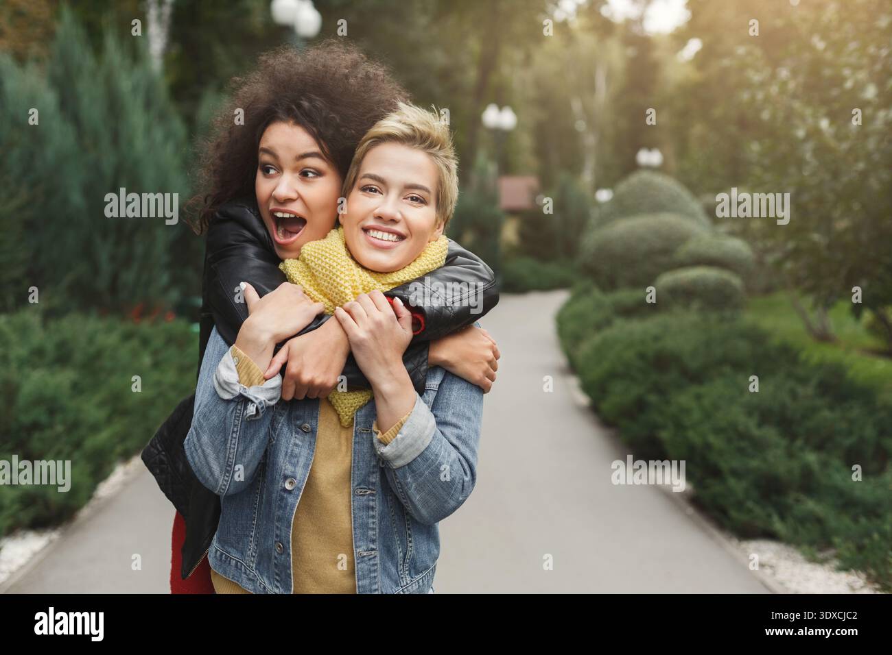 Two Friends Enjoy a Fun Moment While Hugging Each Other in a Park Setting During Daylight Hours Stock Photo
