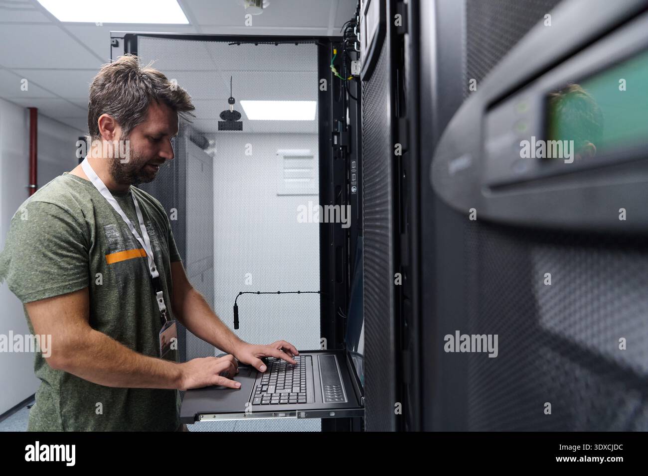 IT technician configuring servers on a rack console in a data center server room Stock Photo