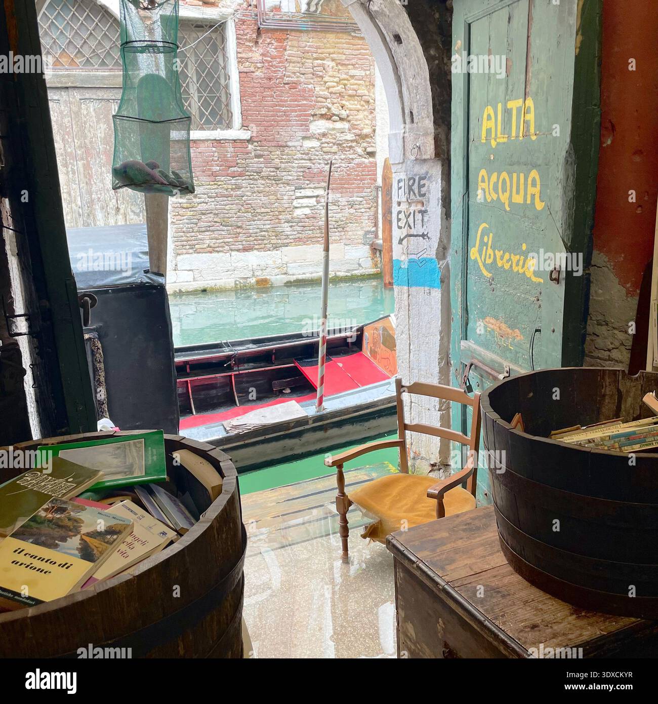 Venice, Italy - March 2 2026: Interior of a small canal-side bookstore in Venice with “alta acqua” flood warning painted on the door and a gondola moo - Smartphone Captured Stock Image