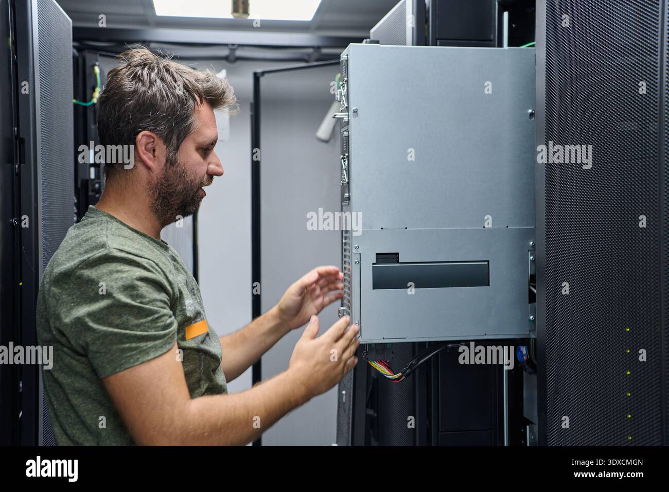 IT technician inspecting and installing server hardware inside a data center equipment rack Stock Photo
