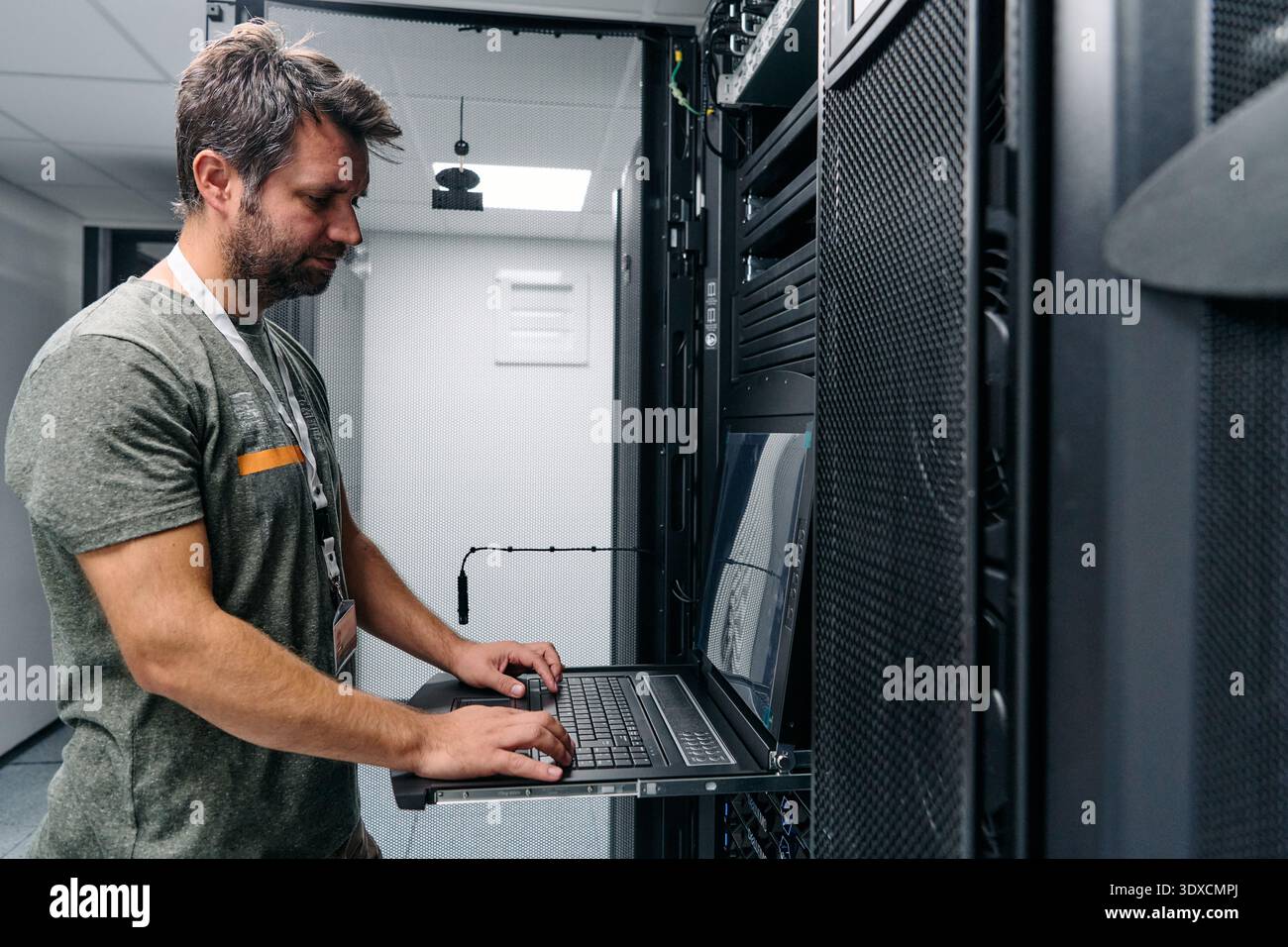 It technician configuring servers on a rack-mounted laptop in a modern data center server room Stock Photo