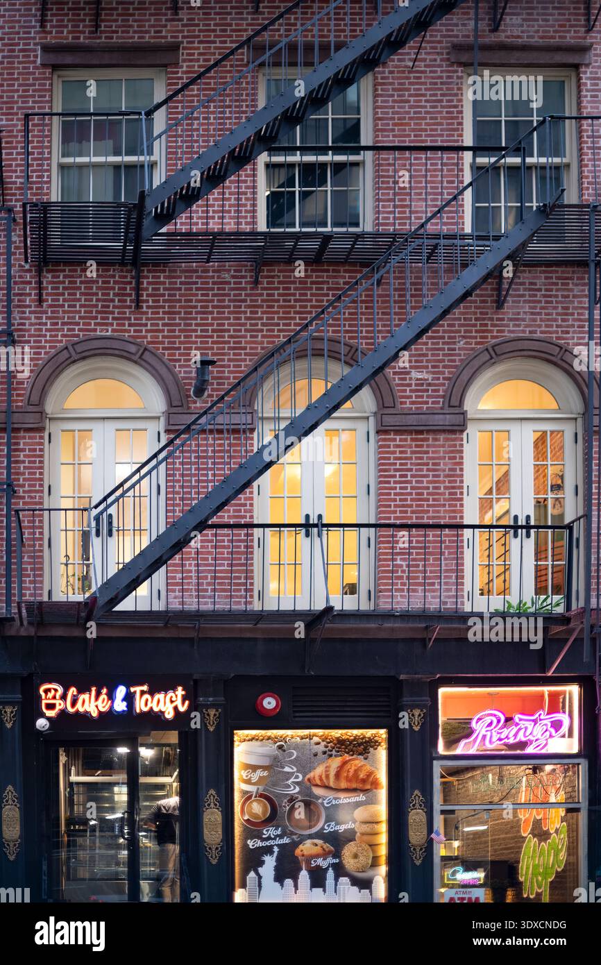 The warm glow of a cafe and local shops illuminates the street level of a historic New York City apartment building. Stock Photo
