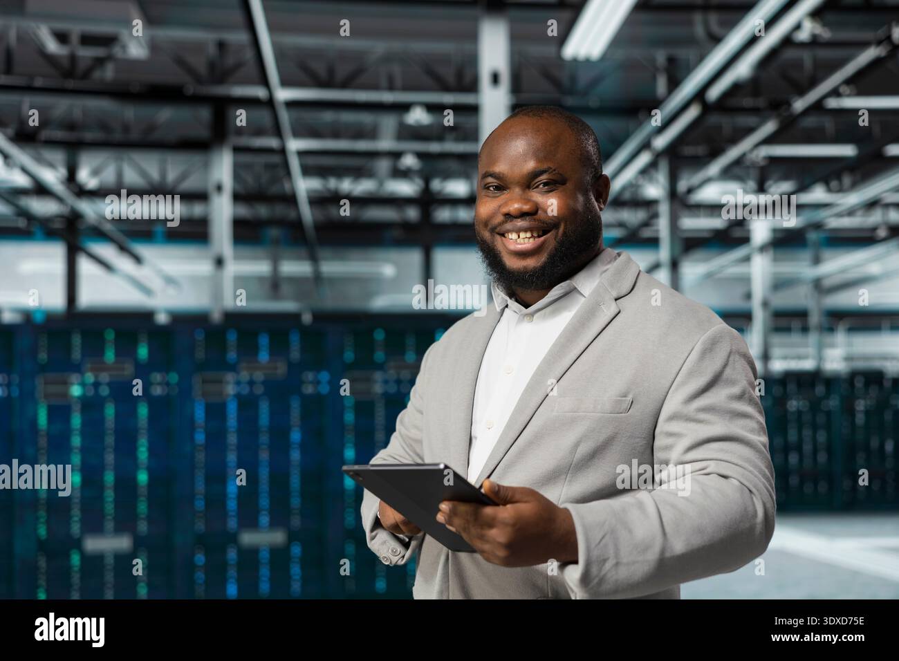 Cheerful engineer in data center updating systems using tablet, protecting equipment from damaging software errors. Happy server farm worker using device, looking for bugs causing gear to slow down Stock Photo