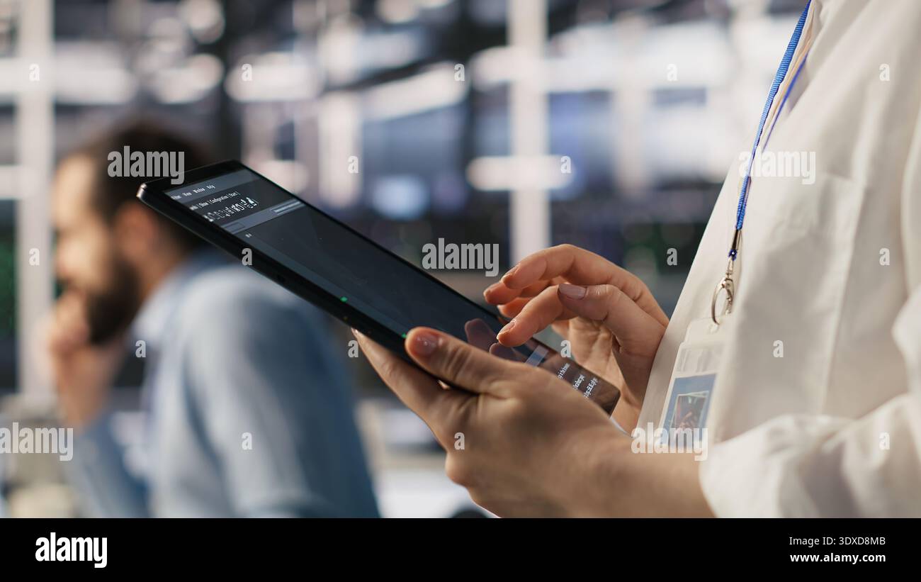 Close up of data center system administrator coding on tablet, doing software updates. Server room IT expert looking at device screen, optimizing infrastructure rackmounts configuration rigs, camera A Stock Photo