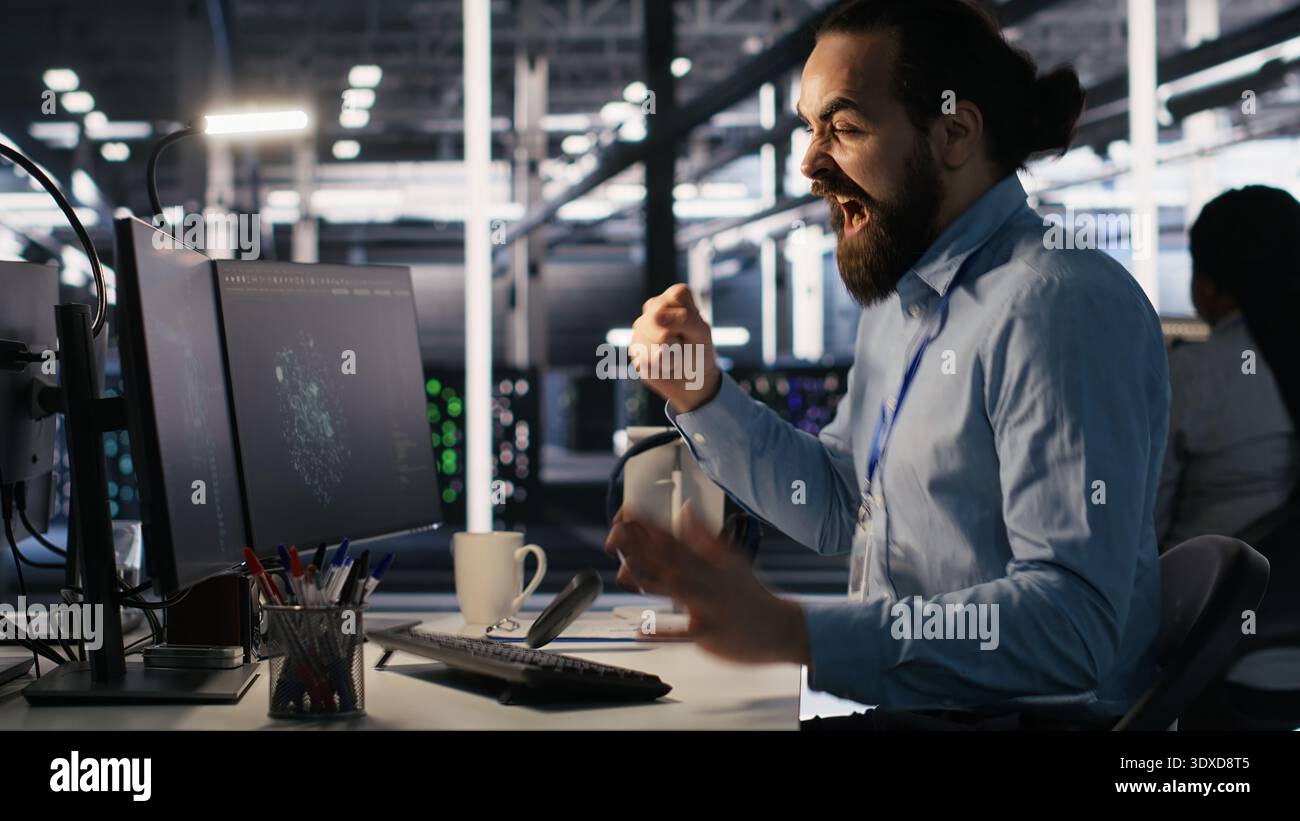 Server room IT specialist frustrated by difficult complex tasks in office. Stressed engineer developing neural network software while working extended hours in data center, camera A Stock Photo