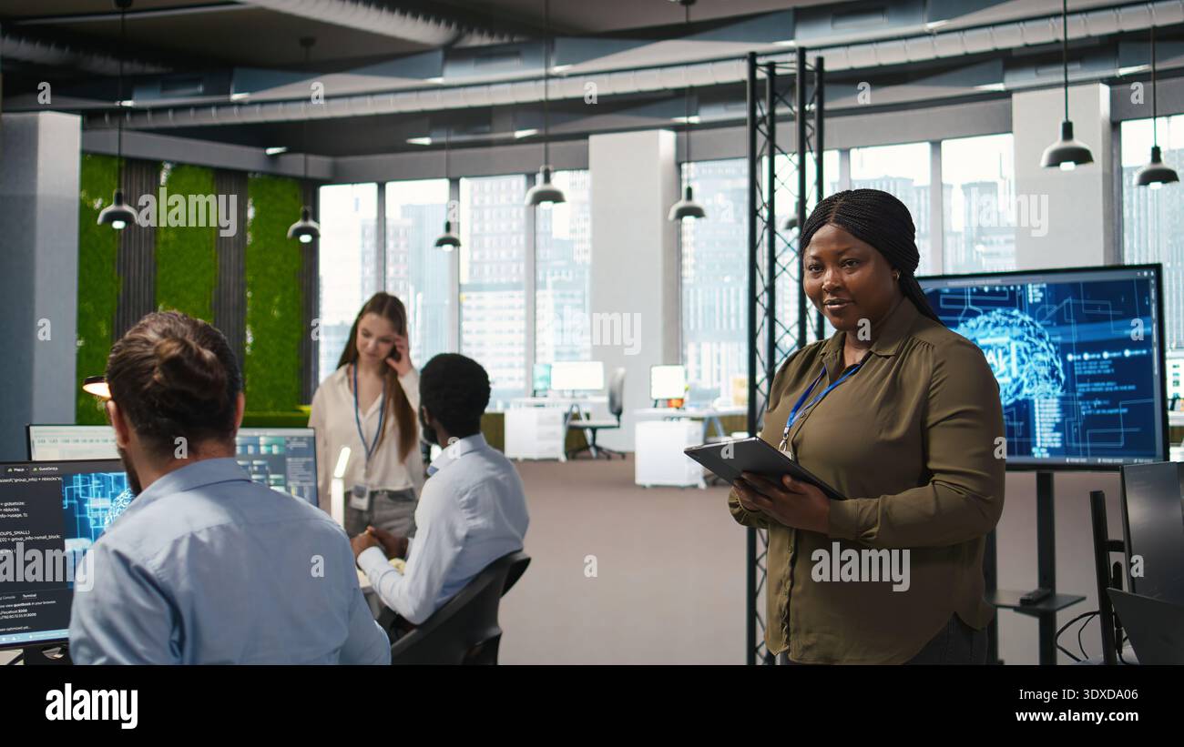 Happy female engineer in office automating repetitive tasks using AI scripts. Jolly african american developer using artificial intelligence to speed up feature implementation, camera A Stock Photo