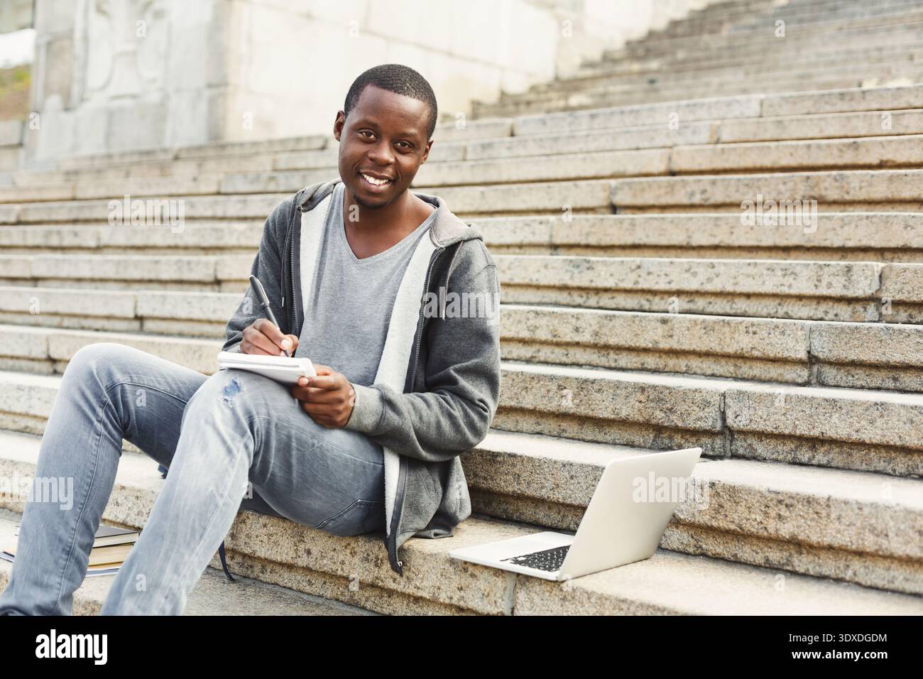 Student Works on Notes in Outdoor Setting Using Laptop and Notebook on Stone Steps Stock Photo