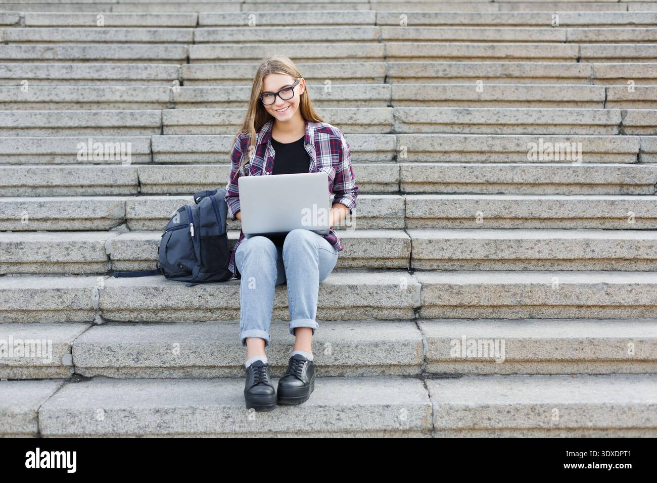 Young Person Sits on Steps Using Laptop to Work on School Tasks or Projects Stock Photo