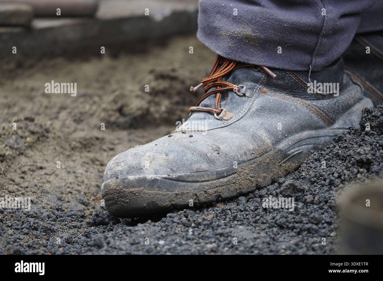 Construction worker stands on dirt with muddy boots Stock Photo