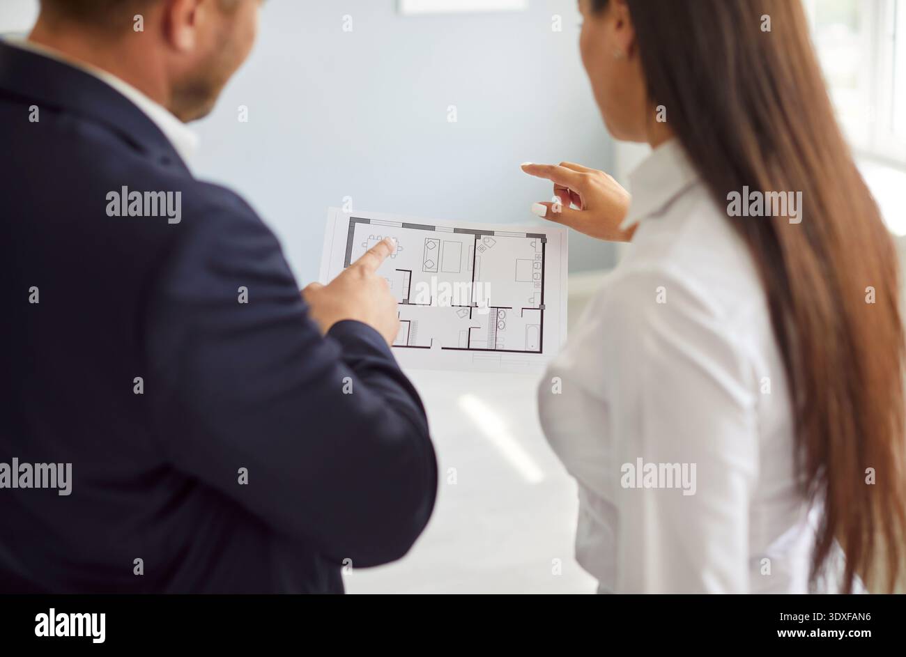 Male engineer, architect or realtor discussing apartment construction plan with young woman client. Stock Photo