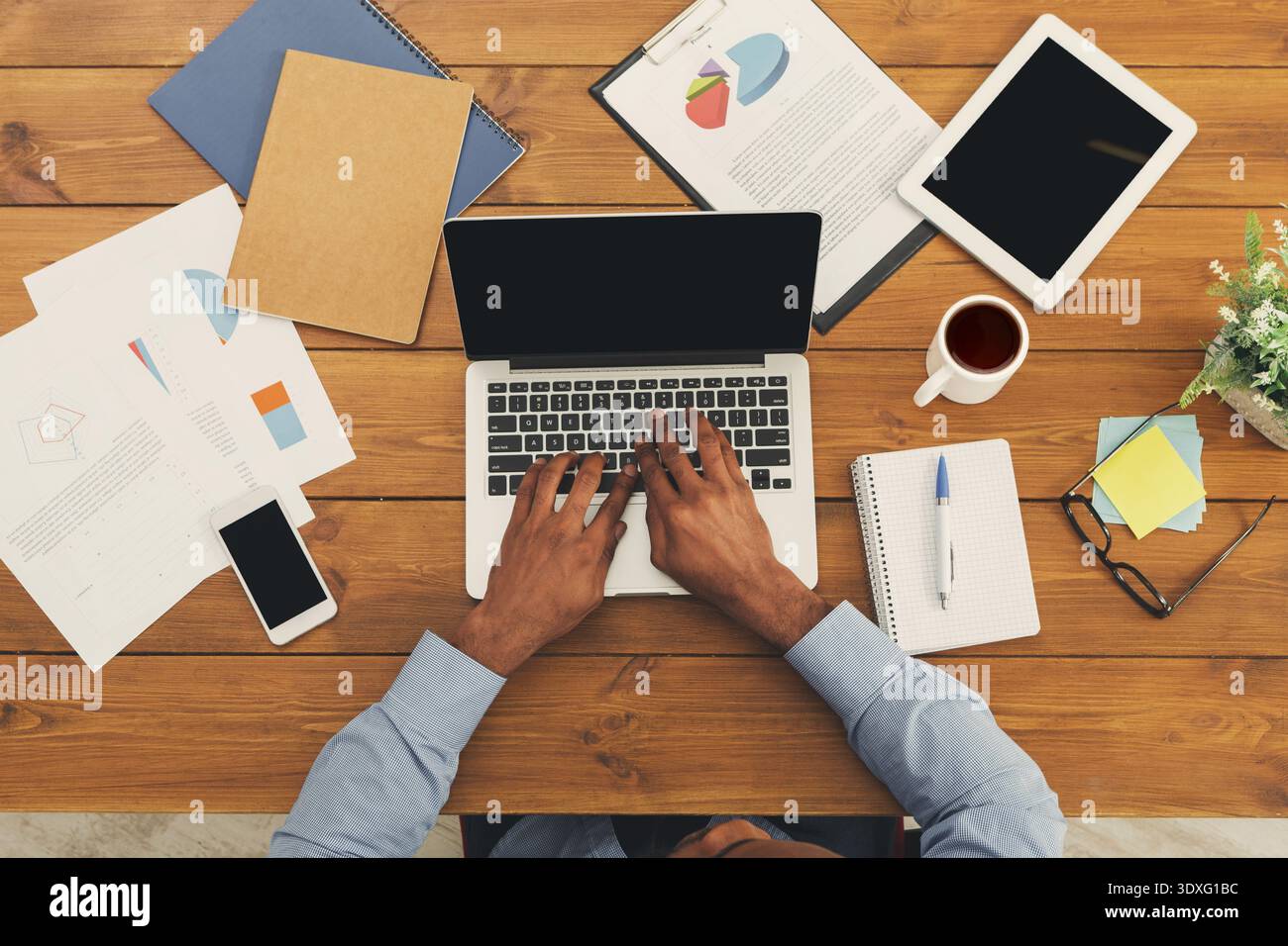 Working on a Laptop in a Workspace With Documents and Tools Around the Table Stock Photo