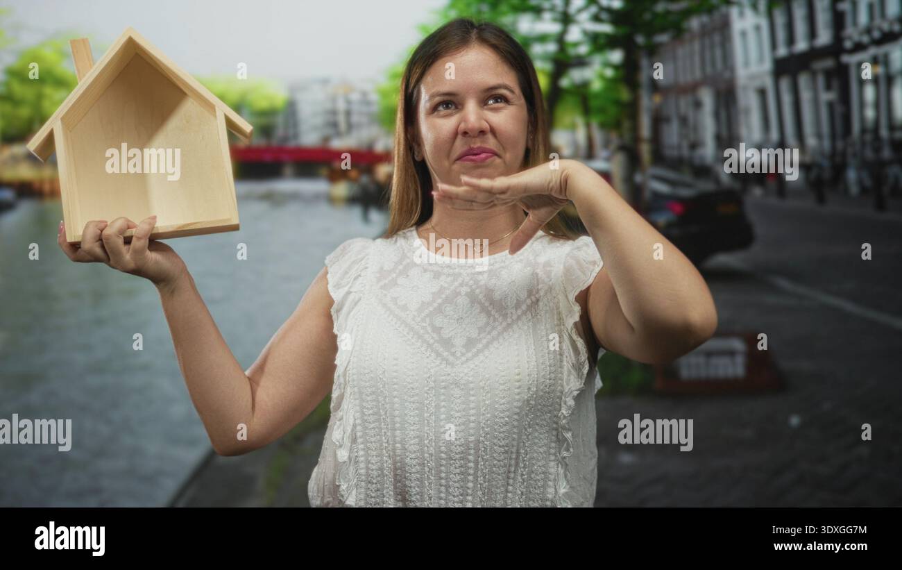 Woman holds small wooden house model in left hand and waves with right ...