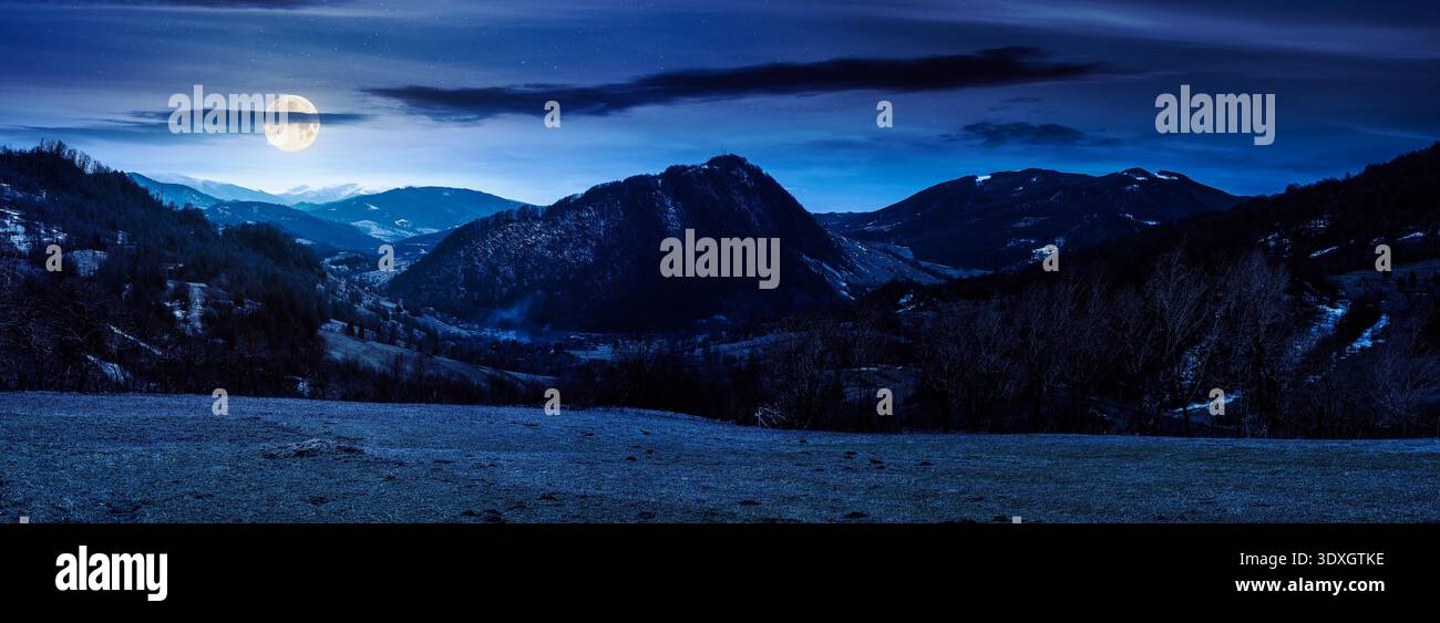 mysterious panorama of a countryside landscape on springtime night. full moon over beautiful view of mountainous rural area from a forested hill. roll Stock Photo