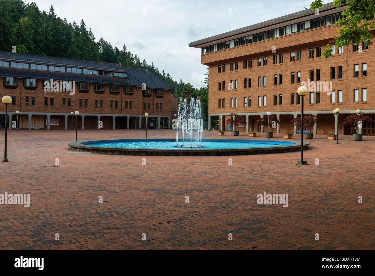 Red Square at Western Washington University, Bellingham, Washington, showing central fountain, brick buildings, and evergreen forest background under Stock Photo