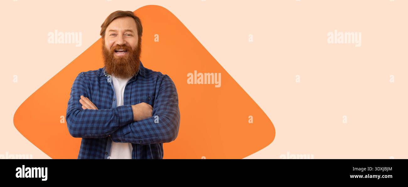 Bearded Man Smiles While Standing Against Orange Background With Crossed Arms Stock Photo