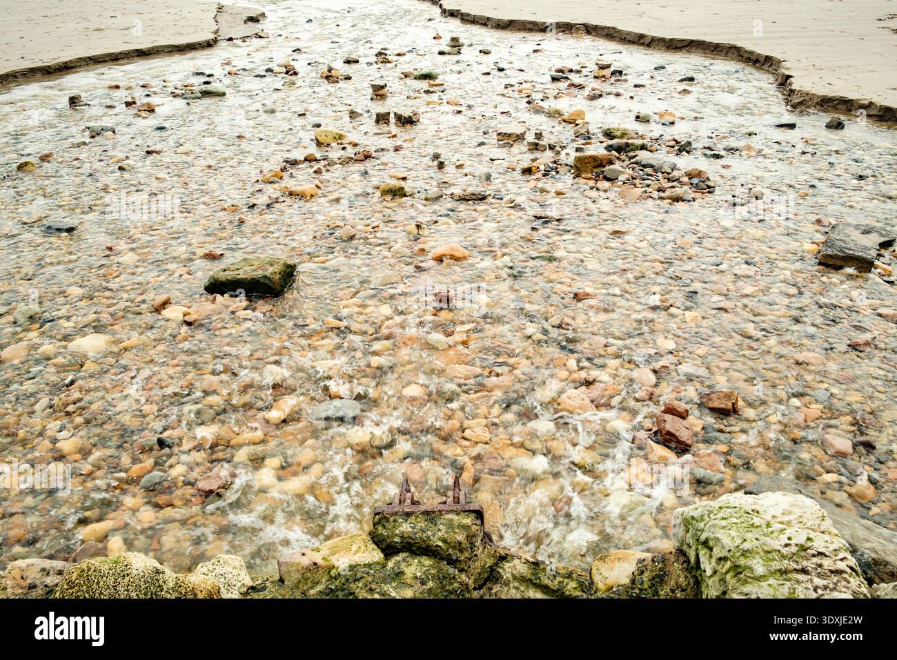 Clear, shallow water flows over a bed of multi-colored pebbles and ...