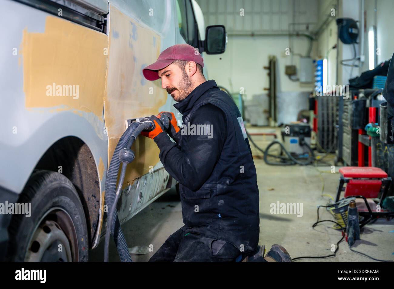 Mechanic sanding van body preparing for paint in repair shop Stock Photo